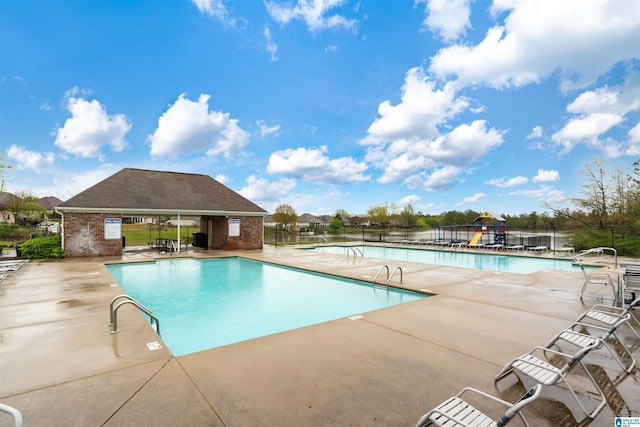 community pool with a patio area, an outdoor structure, and fence