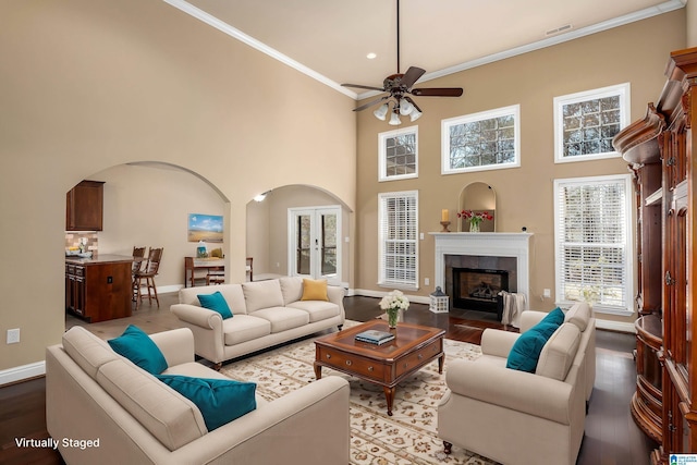 living room featuring wood finished floors, baseboards, visible vents, arched walkways, and ornamental molding