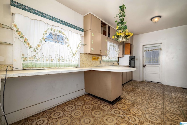 kitchen with baseboards, a peninsula, light countertops, black oven, and backsplash