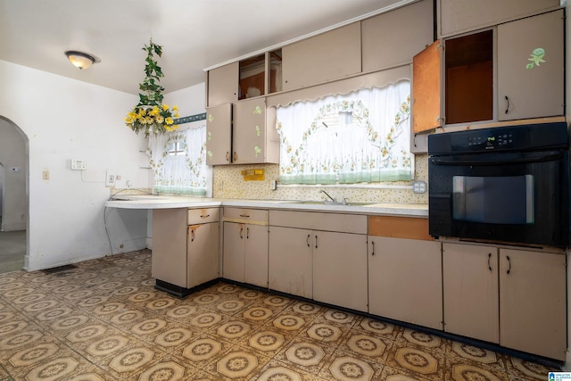 kitchen featuring oven, tasteful backsplash, arched walkways, light countertops, and baseboards