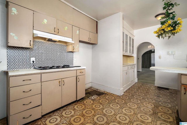 kitchen featuring under cabinet range hood, backsplash, arched walkways, and light countertops