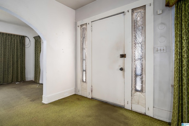 foyer with arched walkways and carpet flooring