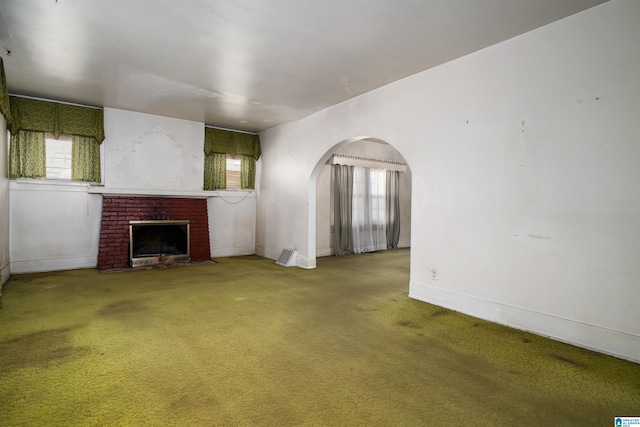 unfurnished living room with a fireplace, carpet, arched walkways, and baseboards