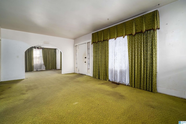 carpeted spare room with visible vents and arched walkways