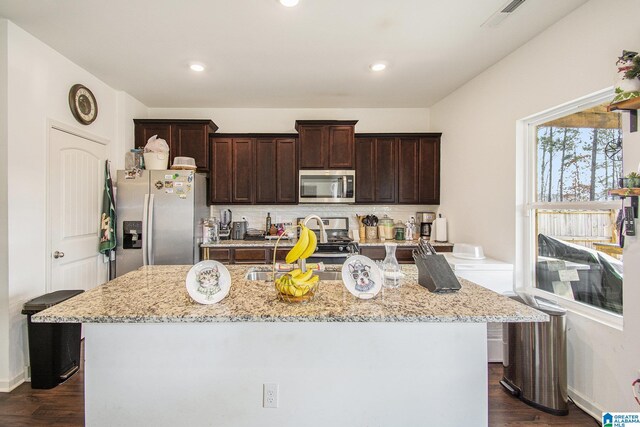 kitchen with decorative backsplash, dark wood-type flooring, a center island with sink, and appliances with stainless steel finishes