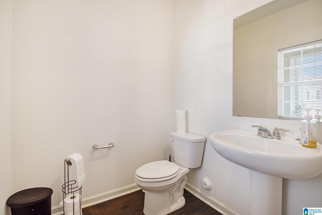 half bathroom featuring toilet, wood finished floors, baseboards, and a sink