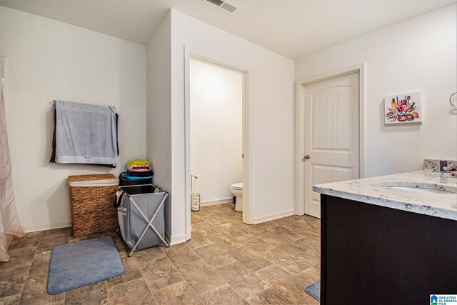 full bath featuring toilet, baseboards, visible vents, and stone finish flooring