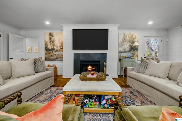 living room with recessed lighting, dark wood-style flooring, a warm lit fireplace, and ornamental molding