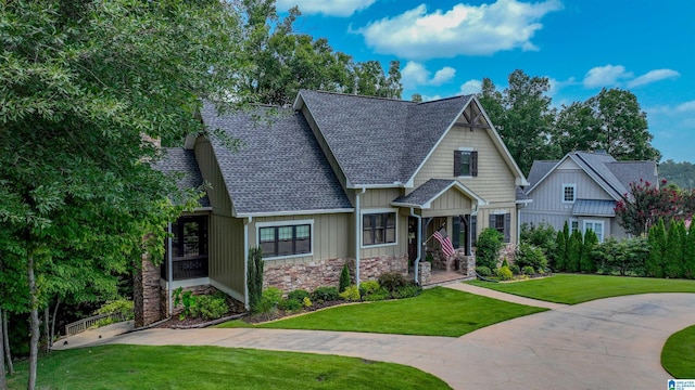 craftsman-style home featuring board and batten siding, a front lawn, stone siding, and a shingled roof