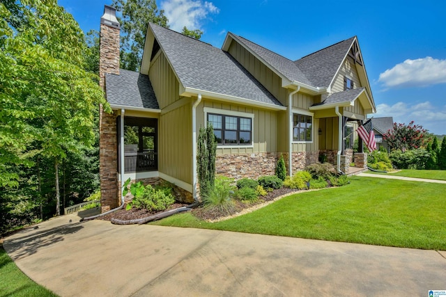 view of front of house featuring board and batten siding, a shingled roof, a front yard, a chimney, and stone siding