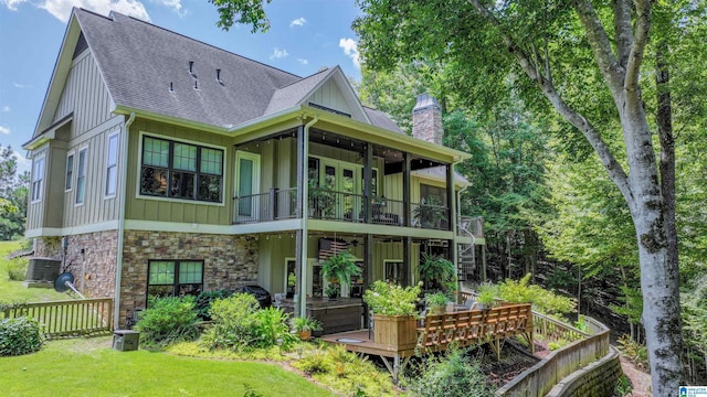 rear view of house featuring a shingled roof, fence, central AC unit, a chimney, and stone siding