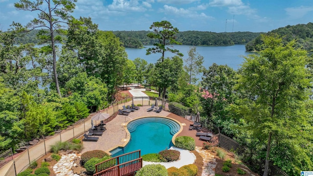 pool featuring a wooded view, a water view, a patio, and fence