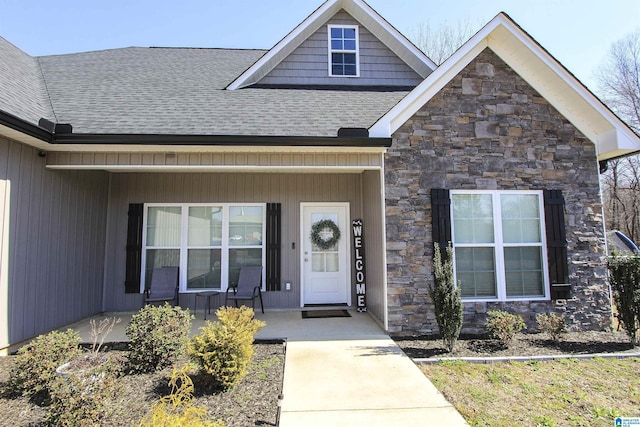 doorway to property featuring stone siding, a porch, and a shingled roof