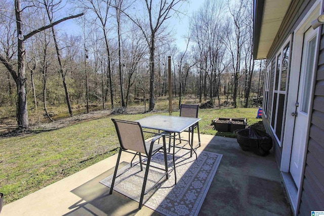 view of patio / terrace featuring outdoor dining space, a wooded view, and a fire pit