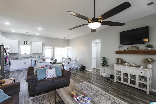 living area featuring visible vents, dark wood-type flooring, ceiling fan with notable chandelier, recessed lighting, and baseboards