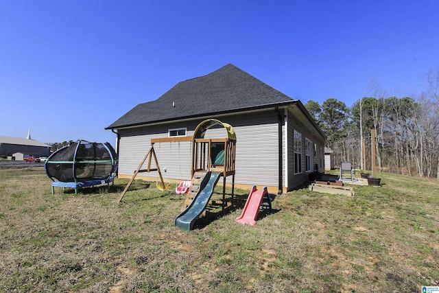 back of house featuring a lawn, a playground, a trampoline, and roof with shingles