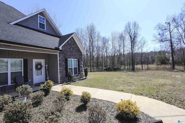 exterior space with a yard, stone siding, and roof with shingles