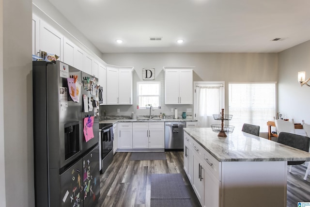 kitchen with dark wood-type flooring, light stone counters, stainless steel appliances, white cabinetry, and a sink