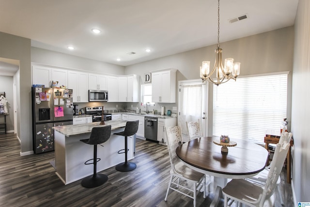 kitchen with visible vents, a kitchen island, stainless steel appliances, white cabinetry, and a sink