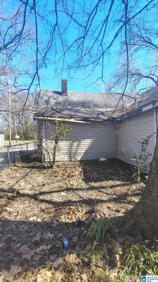 view of side of home featuring roof with shingles, a chimney, and fence