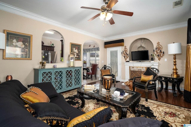 living area with wood finished floors, visible vents, a fireplace, arched walkways, and ornamental molding