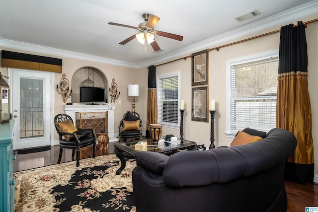 living room with a ceiling fan, wood finished floors, visible vents, a fireplace, and crown molding