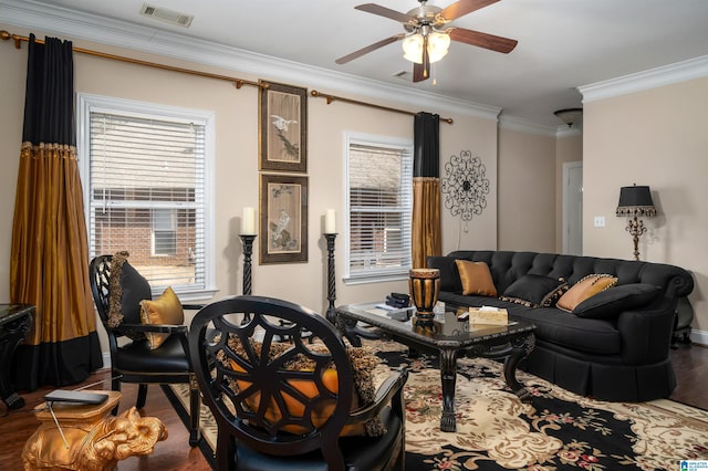 living area with visible vents, crown molding, baseboards, wood finished floors, and a ceiling fan