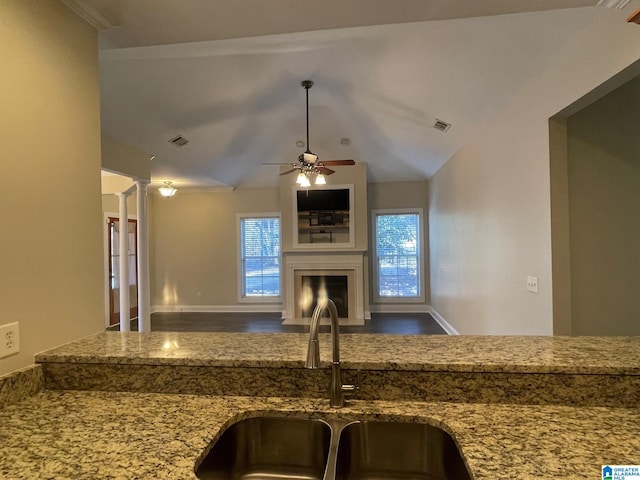 kitchen featuring a fireplace with flush hearth, stone countertops, decorative columns, and a sink