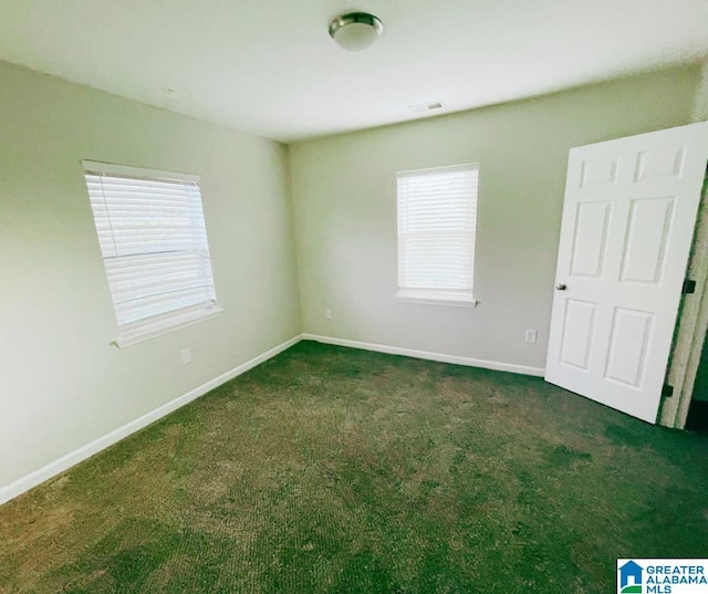 unfurnished room with a healthy amount of sunlight, baseboards, and dark colored carpet