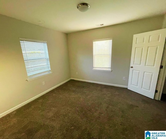 unfurnished room featuring visible vents, baseboards, and dark carpet