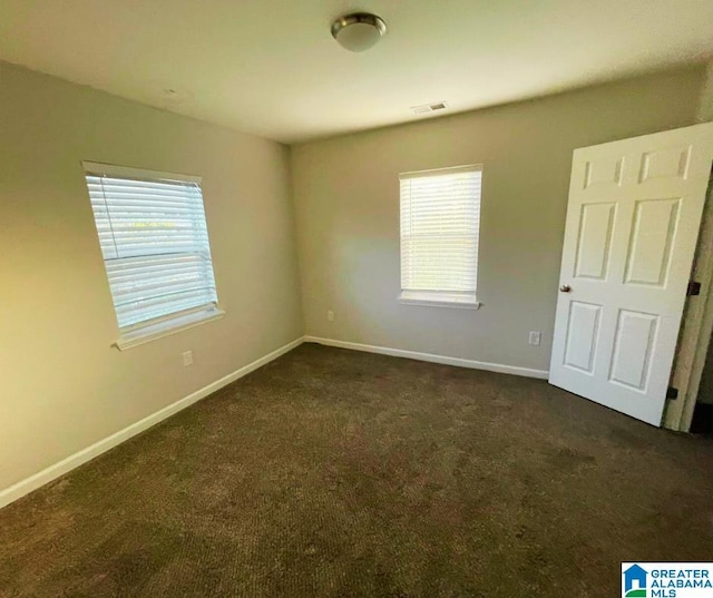 unfurnished room featuring dark colored carpet, visible vents, and baseboards