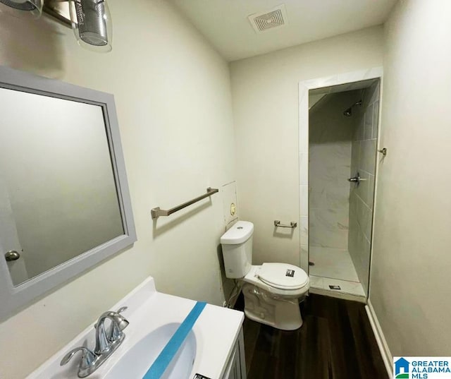 bathroom featuring visible vents, toilet, wood finished floors, and a tile shower