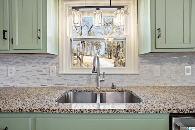 kitchen with decorative backsplash, light stone counters, green cabinetry, and a sink