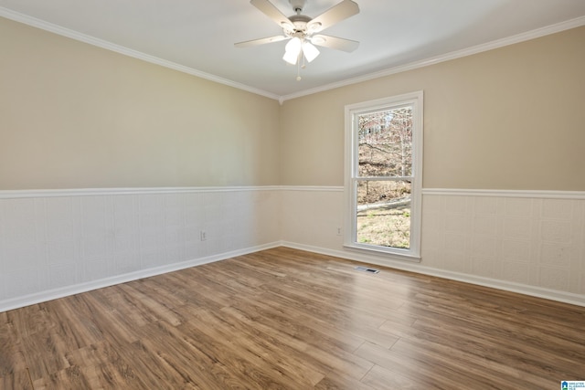 spare room with a wainscoted wall, visible vents, wood finished floors, crown molding, and ceiling fan