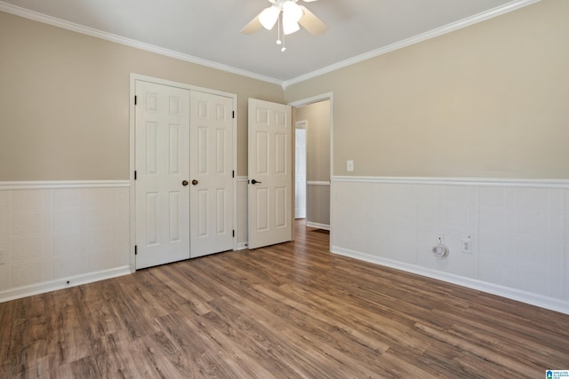 unfurnished bedroom with a closet, wainscoting, ornamental molding, and wood finished floors