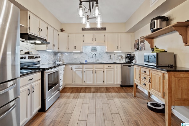 kitchen featuring under cabinet range hood, dark countertops, appliances with stainless steel finishes, and a sink