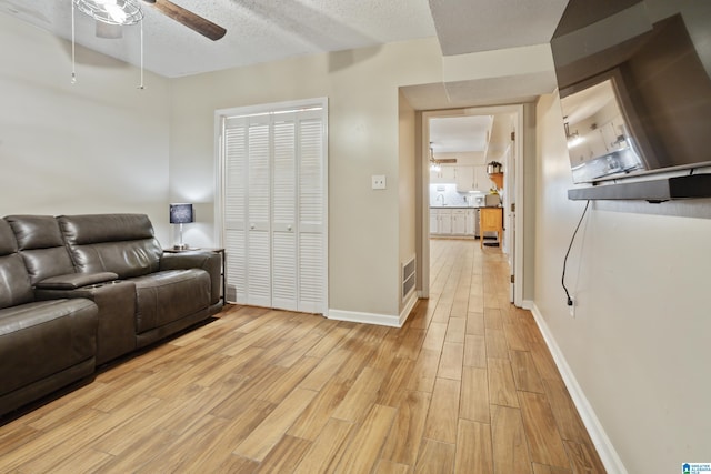 living area featuring baseboards, visible vents, light wood finished floors, and ceiling fan