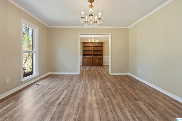 empty room with baseboards, a notable chandelier, wood finished floors, and ornamental molding