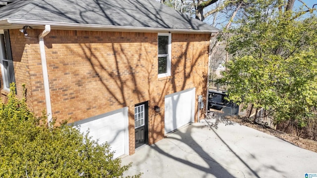 view of side of home featuring brick siding, a garage, and roof with shingles