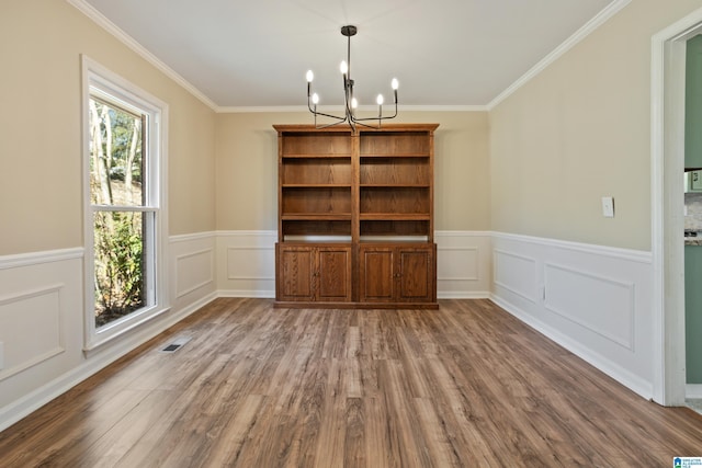 unfurnished dining area featuring crown molding, a decorative wall, a notable chandelier, and wood finished floors