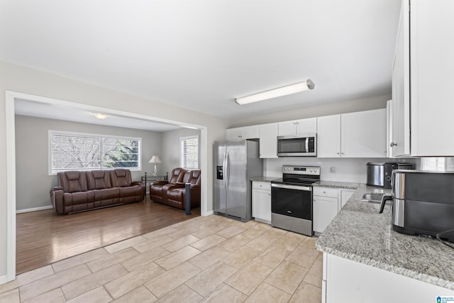 kitchen featuring light stone counters, baseboards, white cabinets, appliances with stainless steel finishes, and open floor plan