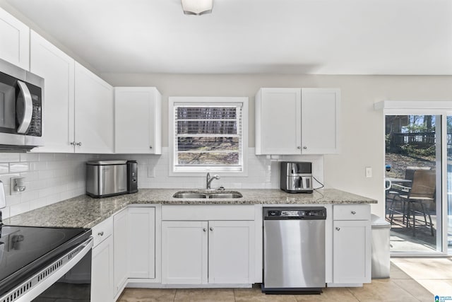 kitchen featuring light stone countertops, decorative backsplash, white cabinets, stainless steel appliances, and a sink