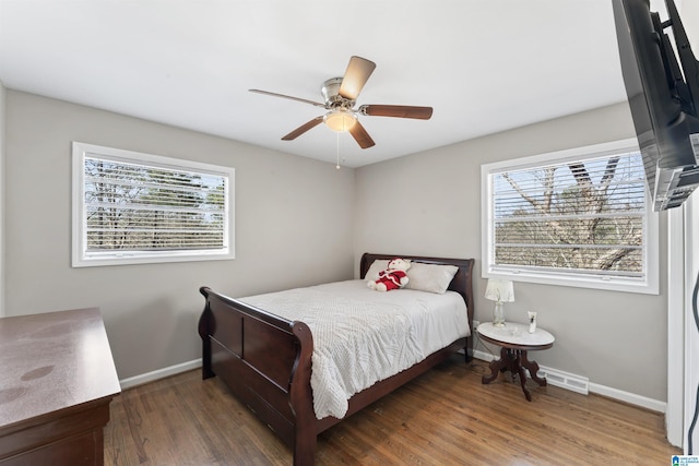 bedroom featuring baseboards, multiple windows, wood finished floors, and a ceiling fan