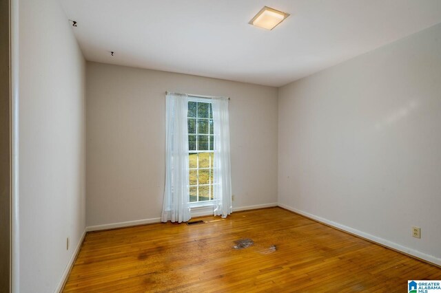 empty room with visible vents, baseboards, and hardwood / wood-style flooring