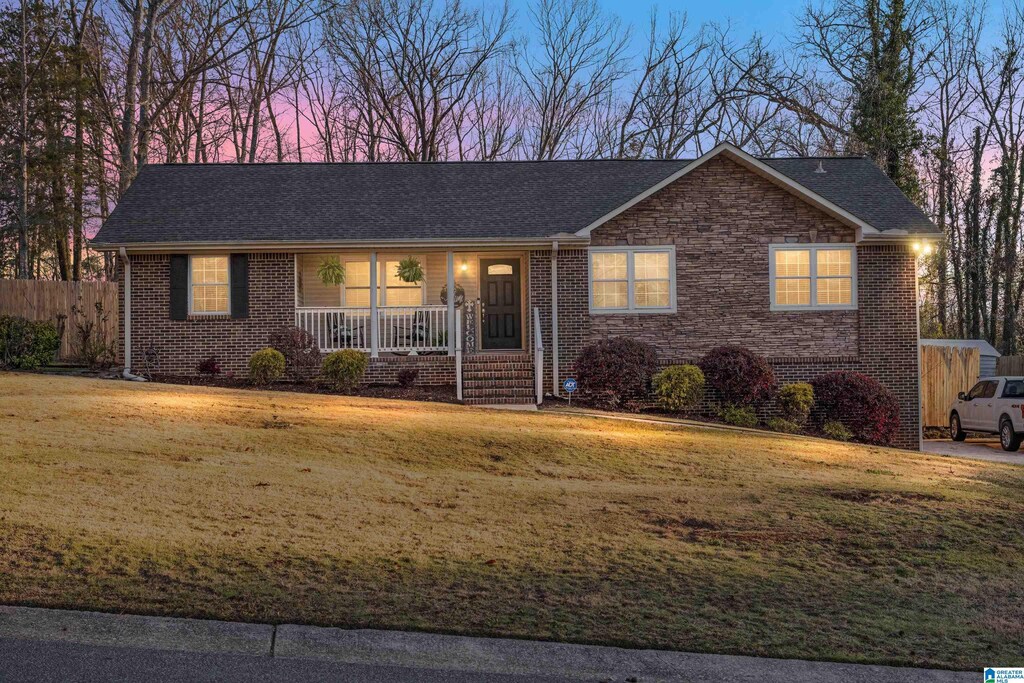 single story home with brick siding, a shingled roof, a front lawn, covered porch, and stone siding