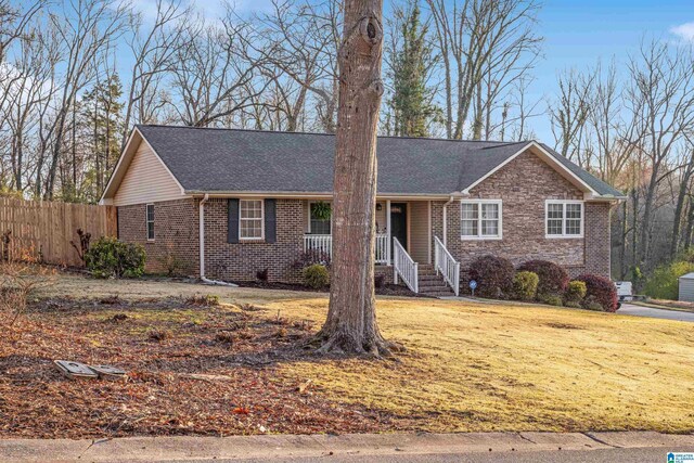 ranch-style home with fence, a porch, a shingled roof, a front lawn, and brick siding