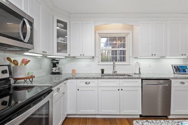 kitchen featuring a sink, stainless steel appliances, glass insert cabinets, white cabinetry, and tasteful backsplash