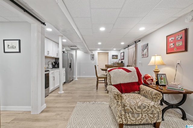 living room featuring baseboards, recessed lighting, a paneled ceiling, a barn door, and light wood-type flooring