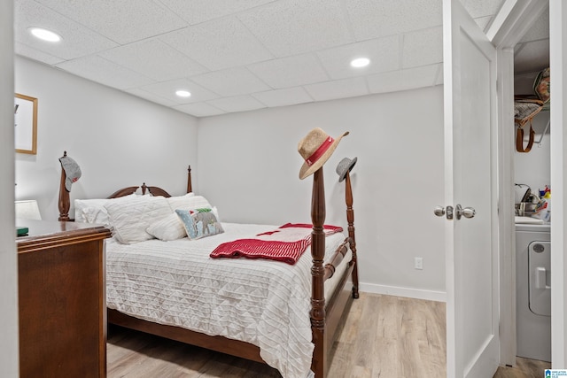 bedroom featuring baseboards, light wood-style flooring, washer / clothes dryer, recessed lighting, and a paneled ceiling