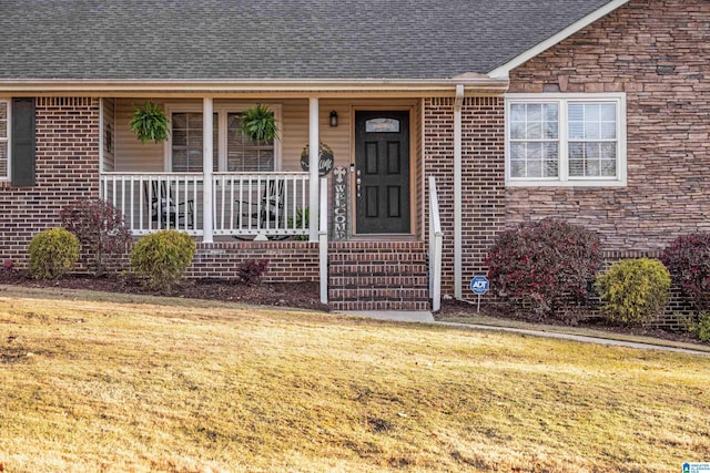 view of exterior entry featuring stone siding, covered porch, a shingled roof, and a lawn